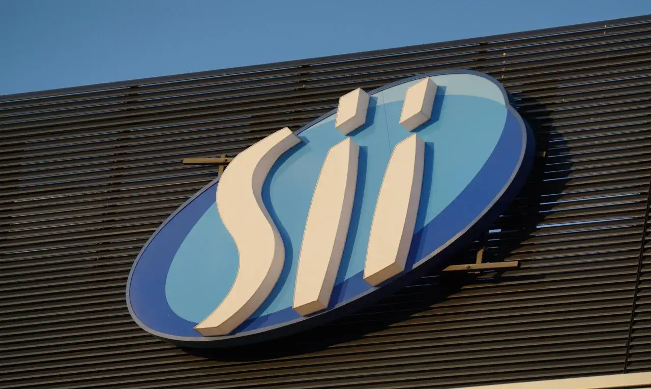 Logo "SII" na niebieskim tle z białymi elementami, na tle ciemnej fasady i nieba.