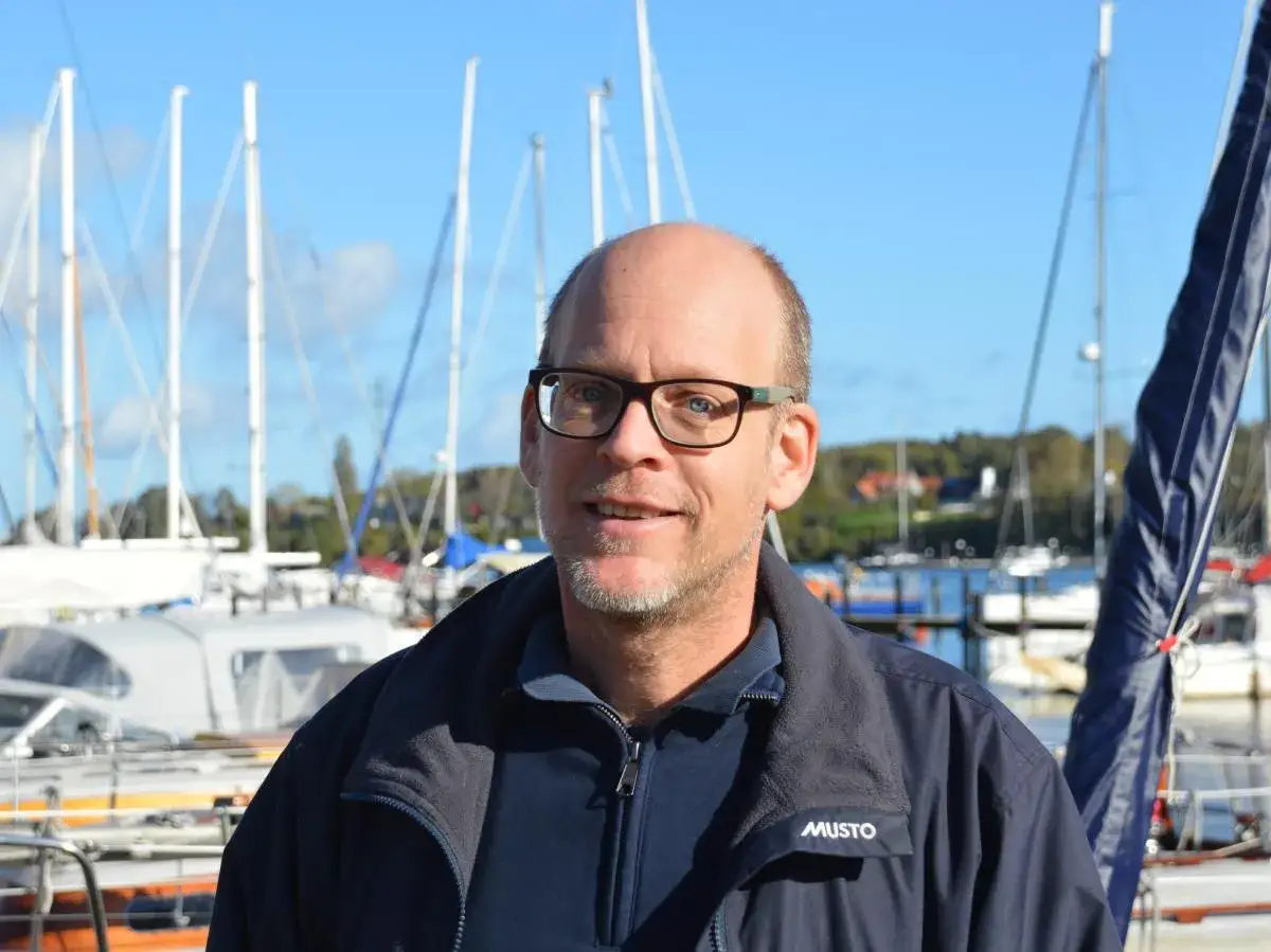 Mann mit Brille lächelt vor Segelbooten. Henningsen und Steckmest sind bereit für die nächste Ausfahrt.