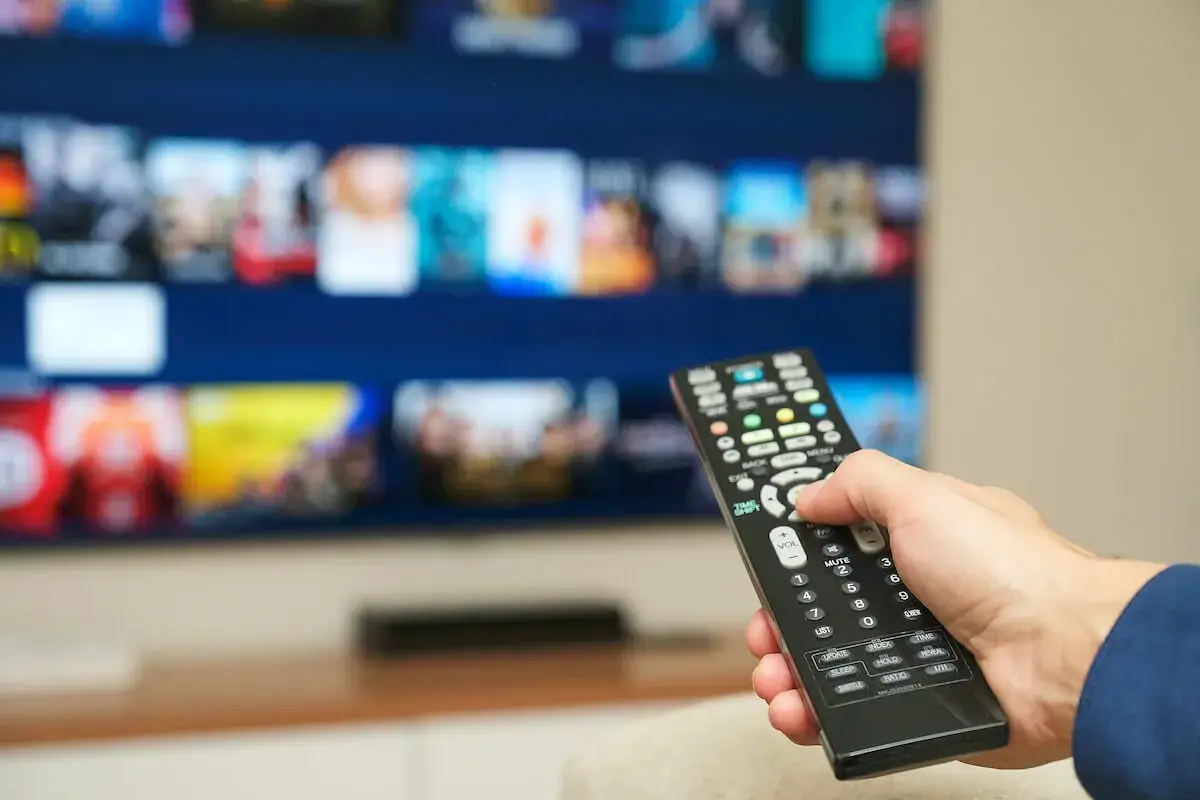 Dłoń trzymająca pilot do telewizora, na ekranie menu platformy streamingowej. Kto płaci abonament RTV w wynajmowanym mieszkaniu?