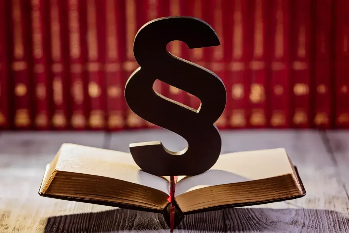 Symbol paragrafu na otwartej księdze, w tle rząd czerwonych ksiąg. Symbolizuje prawo i sprawiedliwość, a może nawet nadzieję na amnestia.