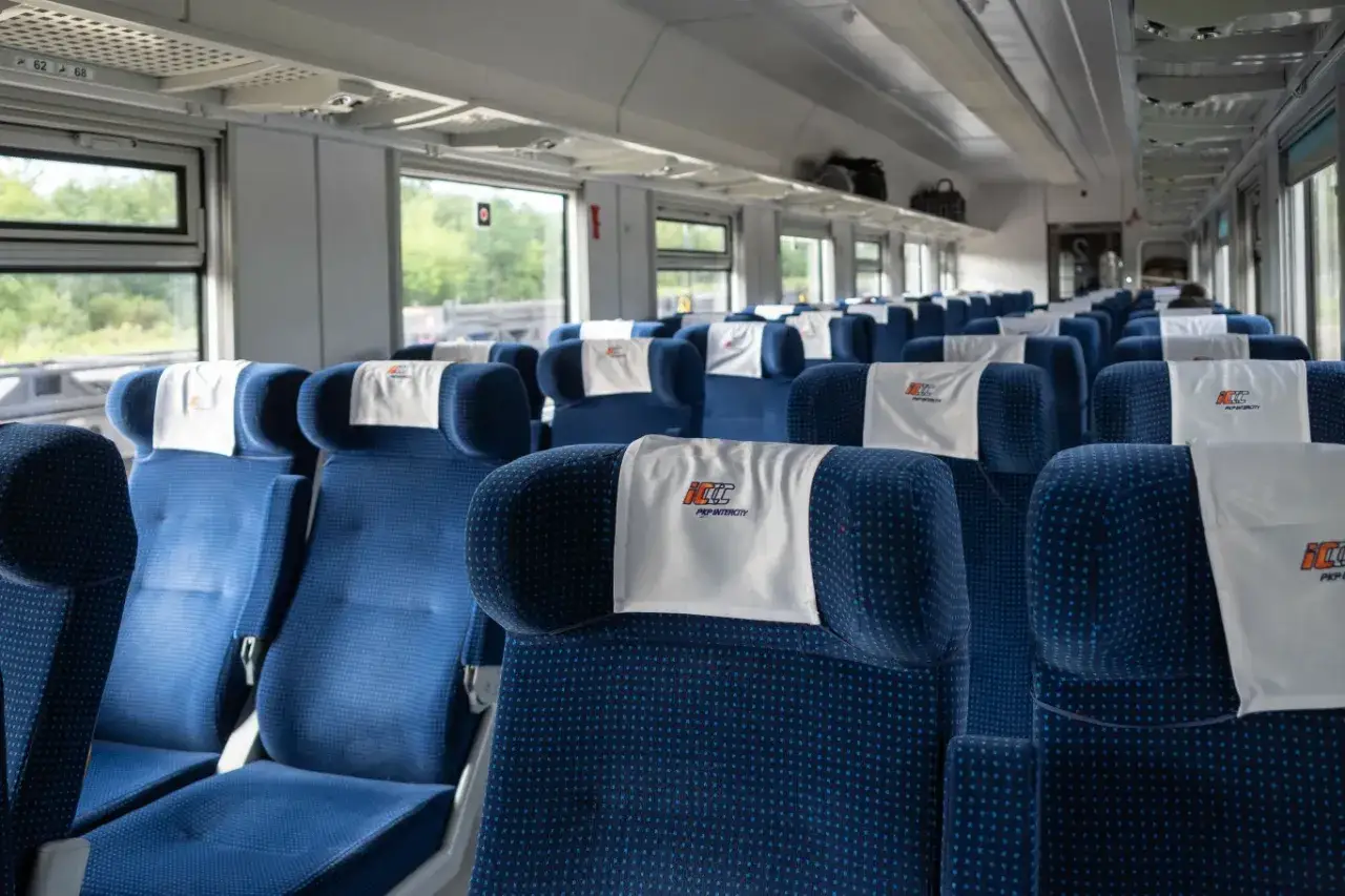 Puste niebieskie siedzenia w wagonie PKP Intercity z zagłówkami z logo.