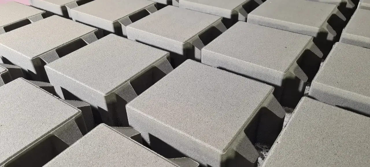 Szare, betonowe kostki brukowe ułożone w rzędach. Różne rodzaje kostki brukowej czekają na ułożenie.