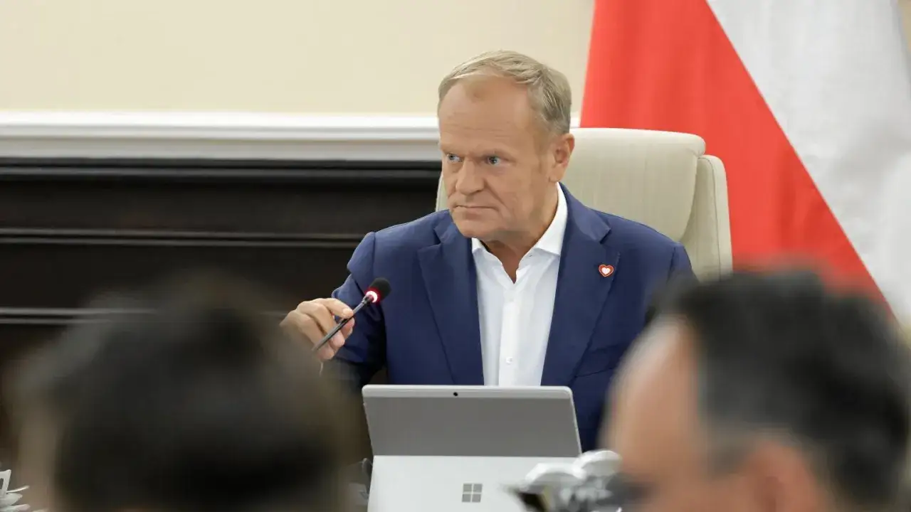 Donald Tusk w Płocku podczas spotkania. Siedzi przy stole z mikrofonem i laptopem.