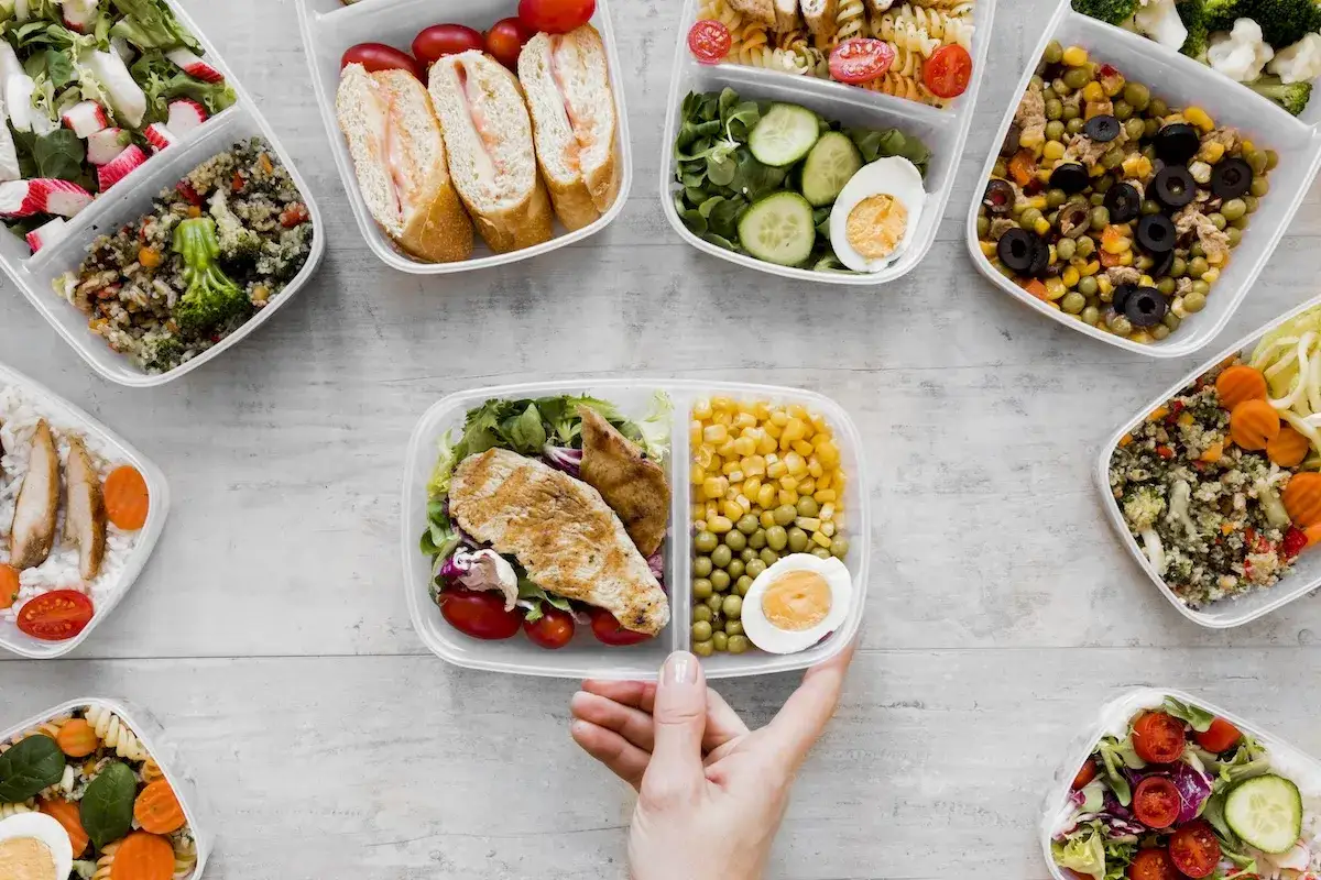 Różnorodne pojemniki z jedzeniem, od sałatek po kanapki i dania z kurczakiem, tworzą apetyczny wybór menu catering.