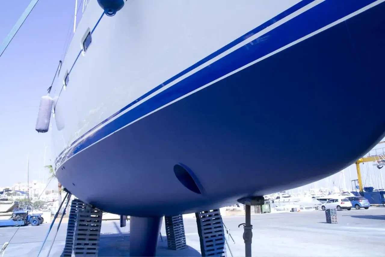 Der blaue **segelboot rumpf** mit weißen Streifen ruht auf Stützen im Hafen.