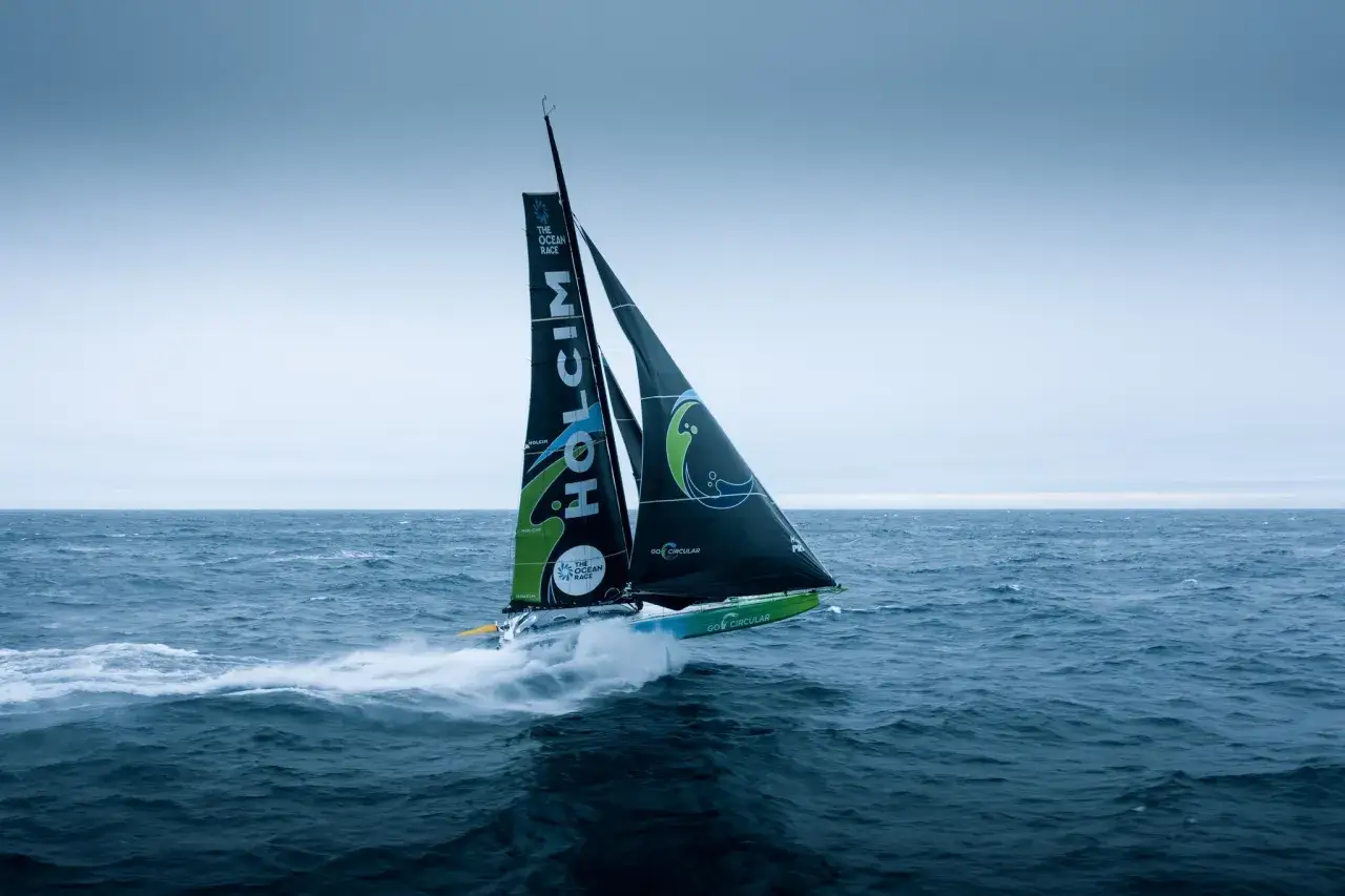 Segelboot des **Team Holcim** pflügt durch die Wellen, die Segel sind mit dem Logo und "The Ocean Race" beschriftet.