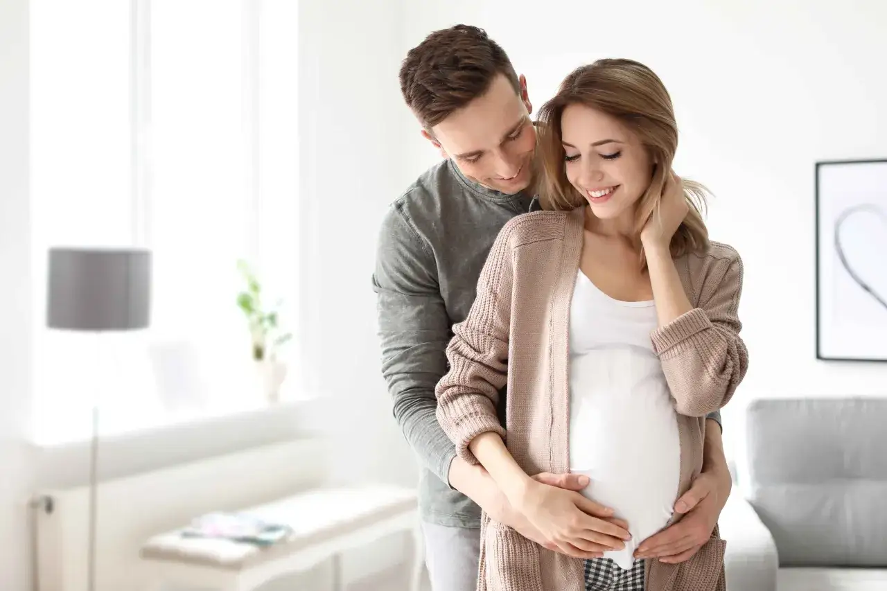 Szczęśliwy mąż obejmuje żonę w ciąży, okazując troskę i miłość. To piękny obraz wsparcia i oczekiwania na dziecko, symbolizujący opiekę na żonę po porodzie.