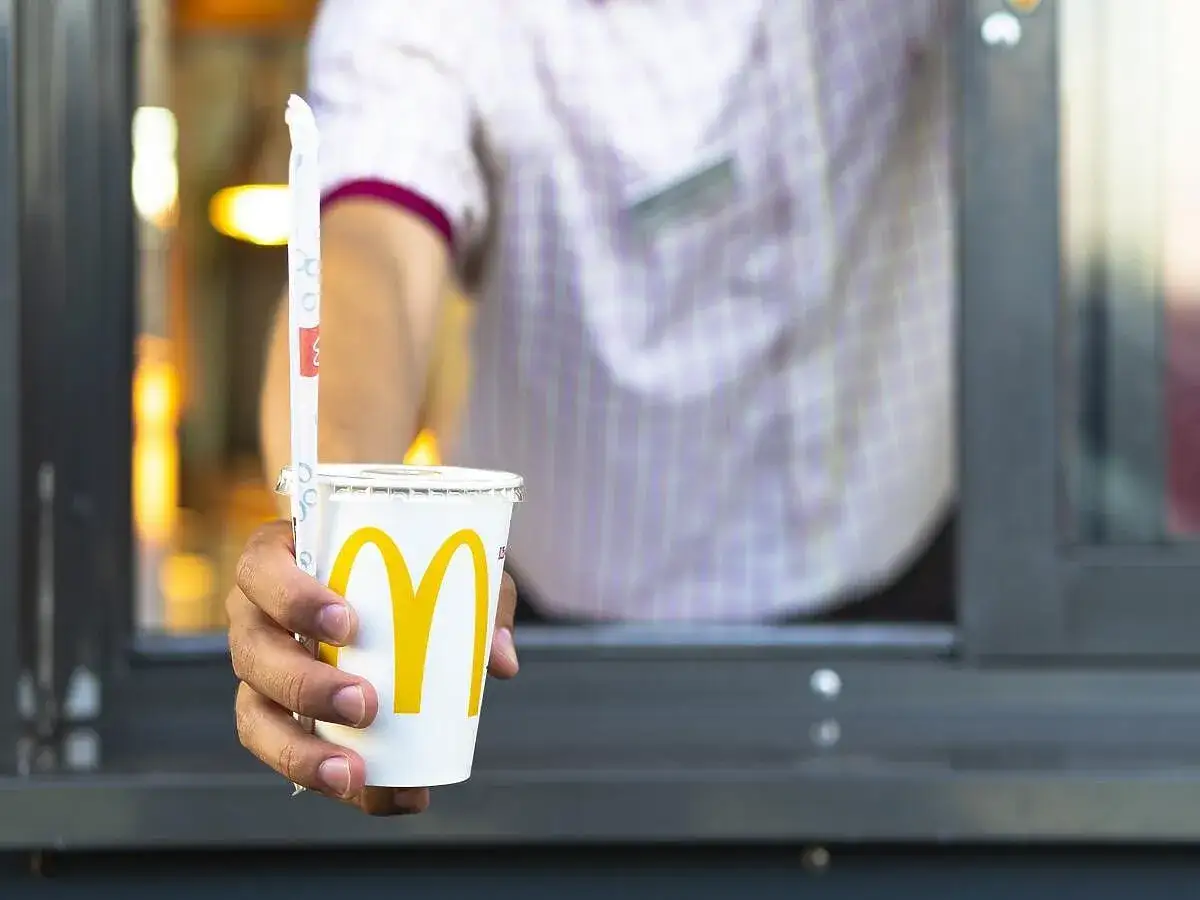 Ręka podaje kubek z McDonald's. Zastanawiasz się, ile kalorii ma cola zero z McDonald's? Ten napój ma zero kalorii.