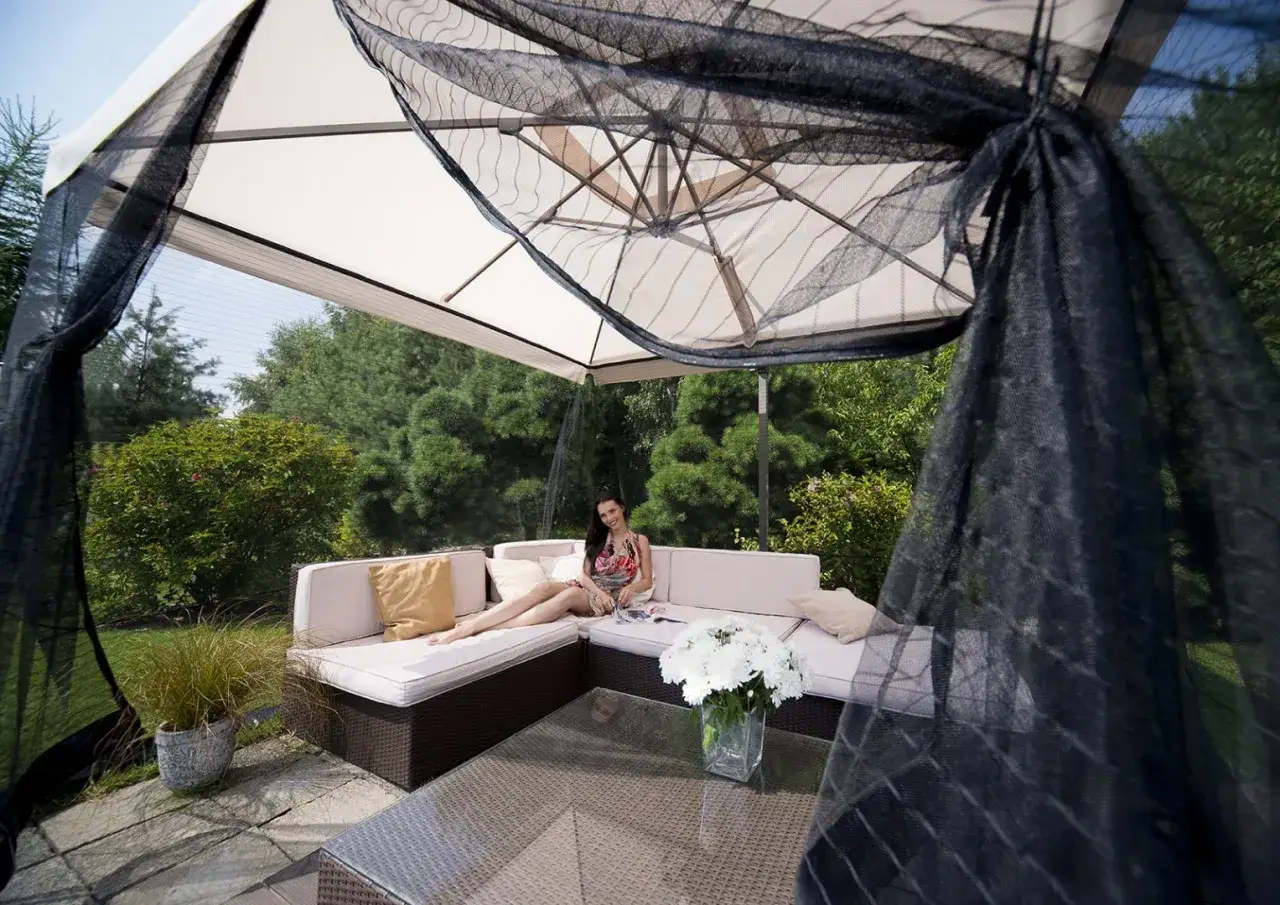 Kobieta relaksuje się na sofie pod dużym parasolem, który chroni przed słońcem i owadami. Idealny parasol na balkon.