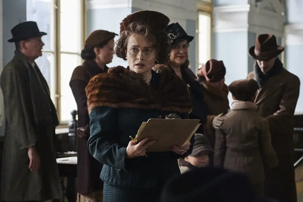 Helena Bonham Carter w filmach, w roli kobiety z tablicą, otoczona ludźmi w strojach z epoki.