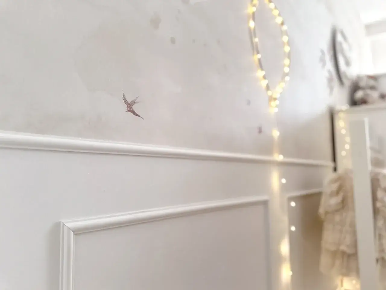 Elegancka sztukateria na ścianie w pokoju dziecka, ozdobiona motywem ptaszka i migoczącymi lampkami.