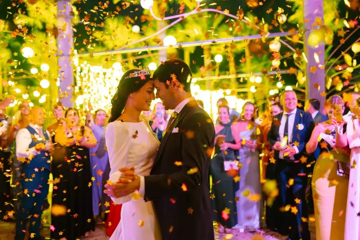 Pareja bailando bajo confeti dorado, rodeada de invitados sonrientes. Una celebración de bridal shower llena de alegría y luces.