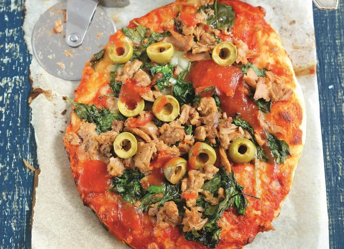 Pyszna pizza z tuńczykiem, szpinakiem i oliwkami, gotowa do pokrojenia.