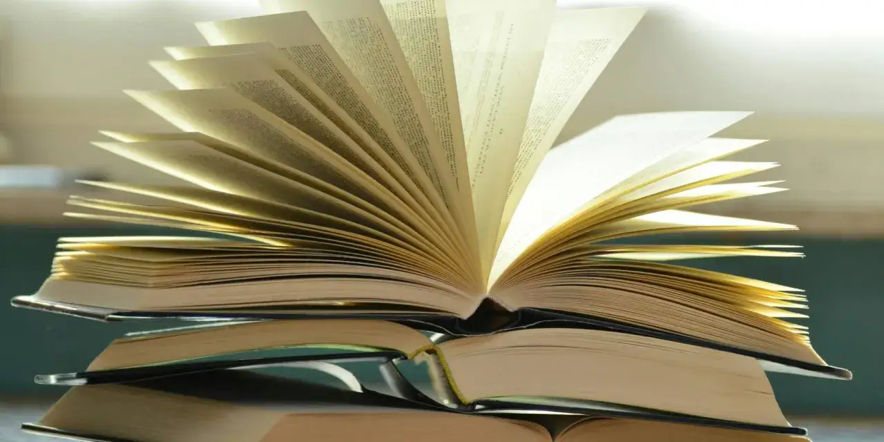 Otwarta książka na stosie innych. Różnica między romansem a literaturą obyczajową z wątkiem miłosnym jest jak między stronami tej książki – subtelna, lecz znacząca.