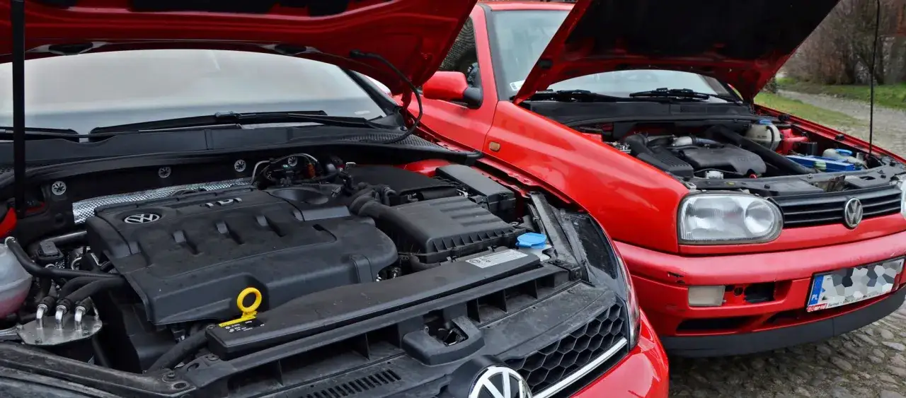 Dwa czerwone Volkswageny z otwartymi maskami. Widać silnik TDI, czyli silnik diesla, w nowszym modelu i starszy silnik w Golfie III.
