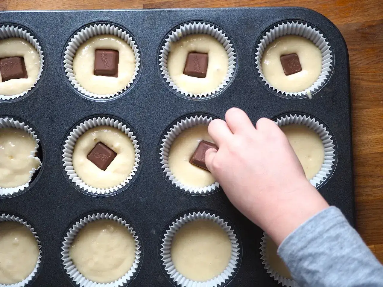 Dziecko wkłada kostkę czekolady do ciasta na muffinki. Prosty sposób, jak udekorować muffinki, by były pyszne.