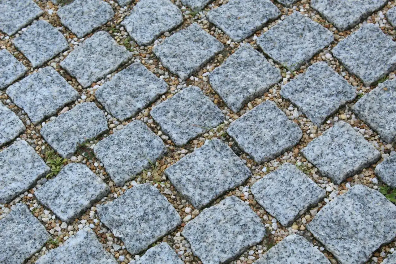 Szara kostka granitowa ułożona na podsypce. Widać, ile podsypki pod kostkę na m2 jest potrzebne do stabilnego ułożenia.