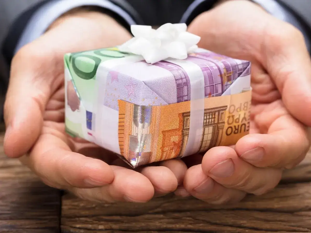 Dłonie trzymają prezent opakowany w banknoty euro. To pomysł, jak zapakować pieniądze na prezent dla dziecka, tworząc unikalną niespodziankę.