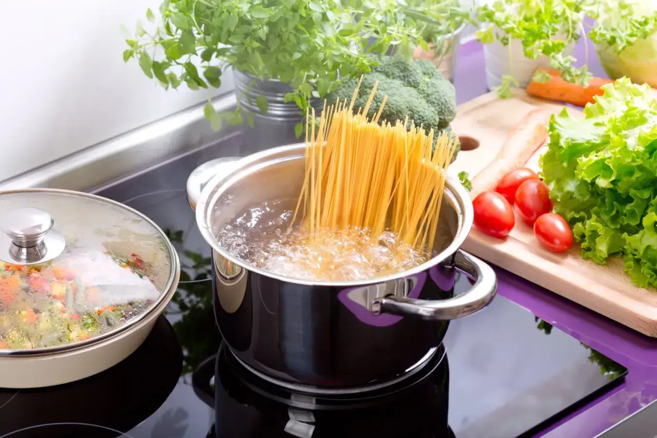 Gotujesz spaghetti? Sprawdź, ile makaronu na porcję, by nikt nie był głodny. Na kuchence wrze woda, a obok czekają świeże warzywa.