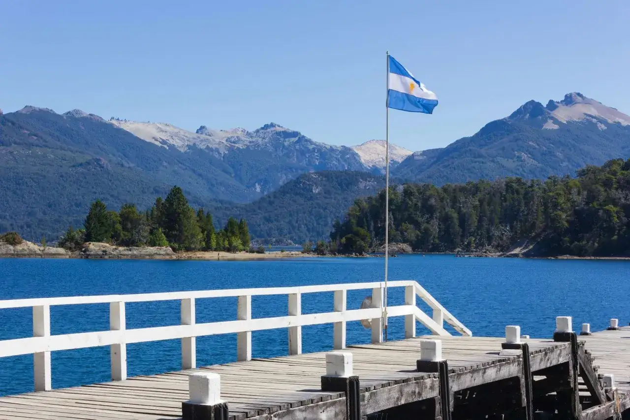 Widok na jezioro i góry w Argentynie, z białą drewnianą przystanią i flagą Argentyny. Czy Argentyna jest bezpieczna? Tak, to piękny kraj.
