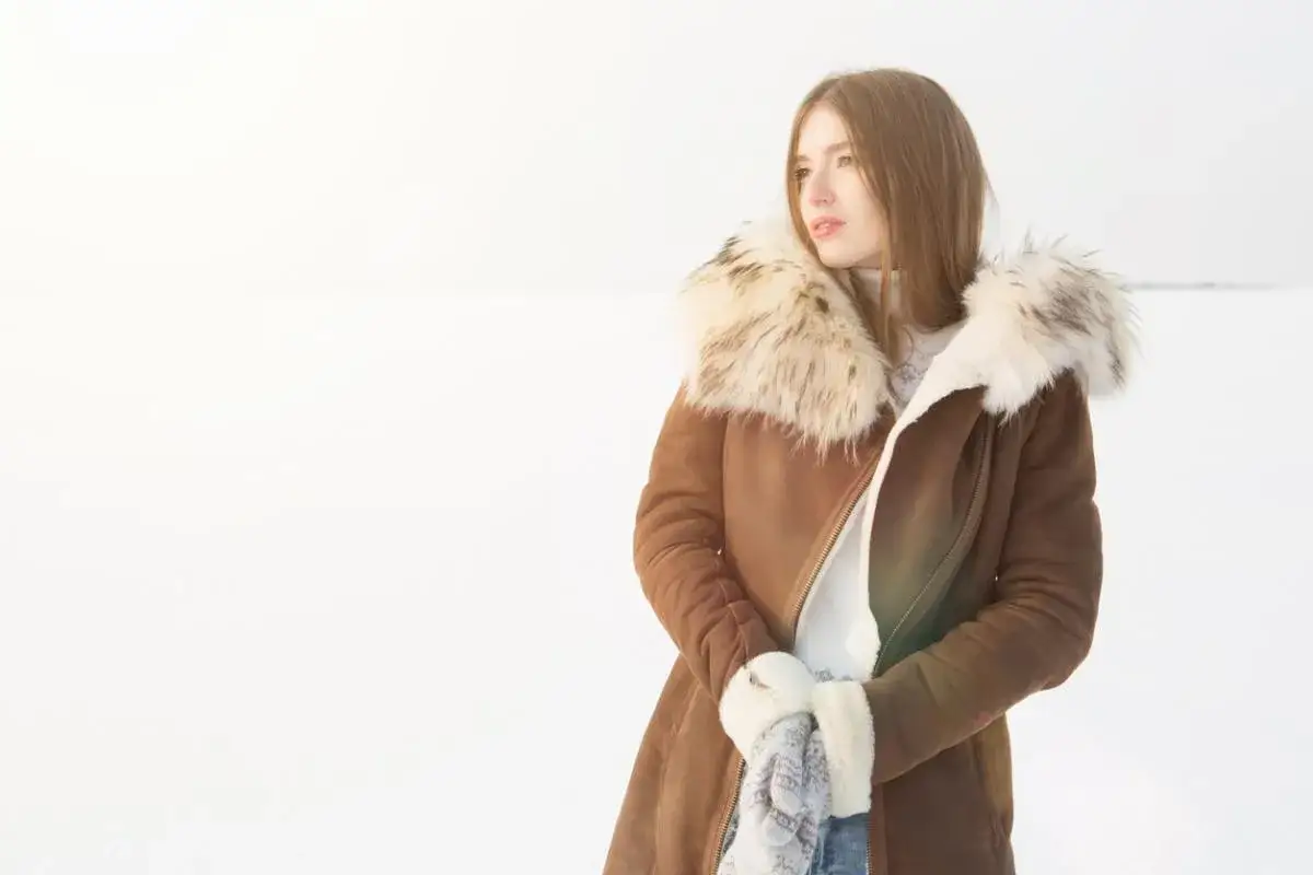 Mujer con abrigo de pelo natural en la nieve, lista para limpiar su ropa de invierno.