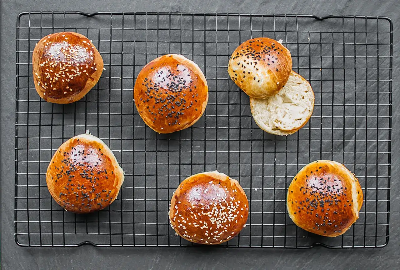 Pięć złotych bułek do burgerów, niektóre posypane sezamem, jedna przekrojona. Idealne, by dowiedzieć się, jak podgrzać bułkę do burgera.