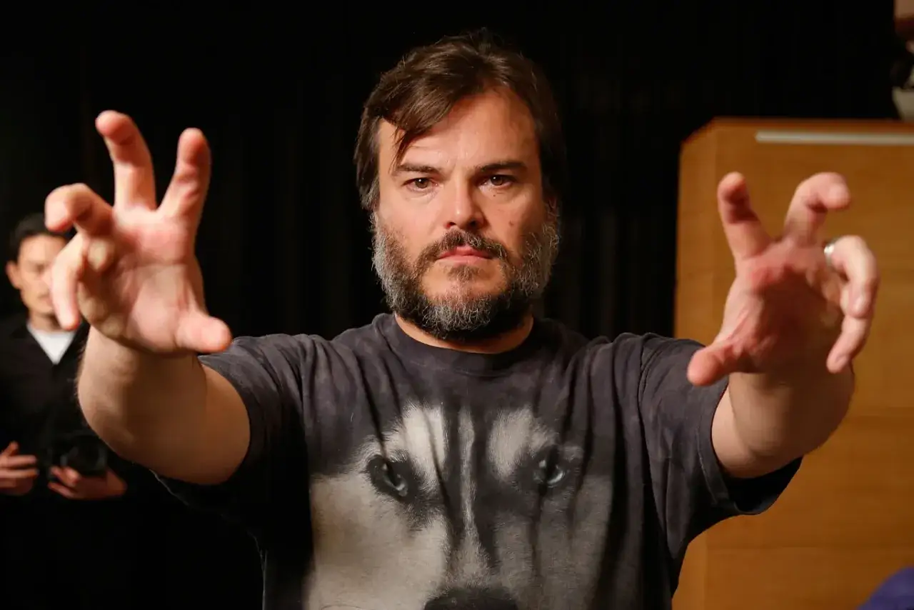 Jack Black w koszulce z wilkiem, z wyciągniętymi rękami. Ciekawe, ile lat ma Jack Black, gdy tak energicznie gestykuluje?