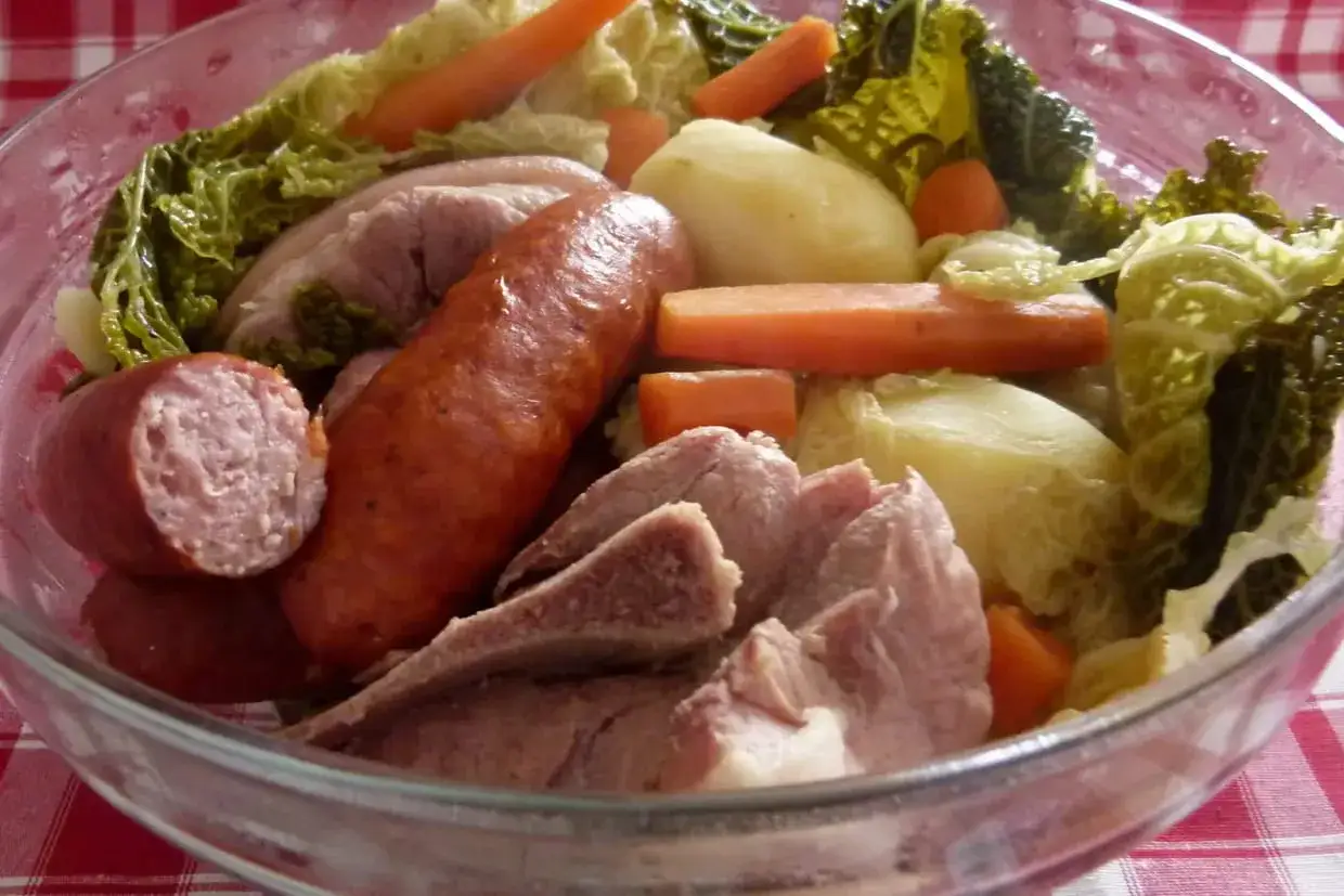 Un plat traditionnel auvergnat généreux : saucisse, porc, chou, carottes et pommes de terre dans un saladier en verre.
