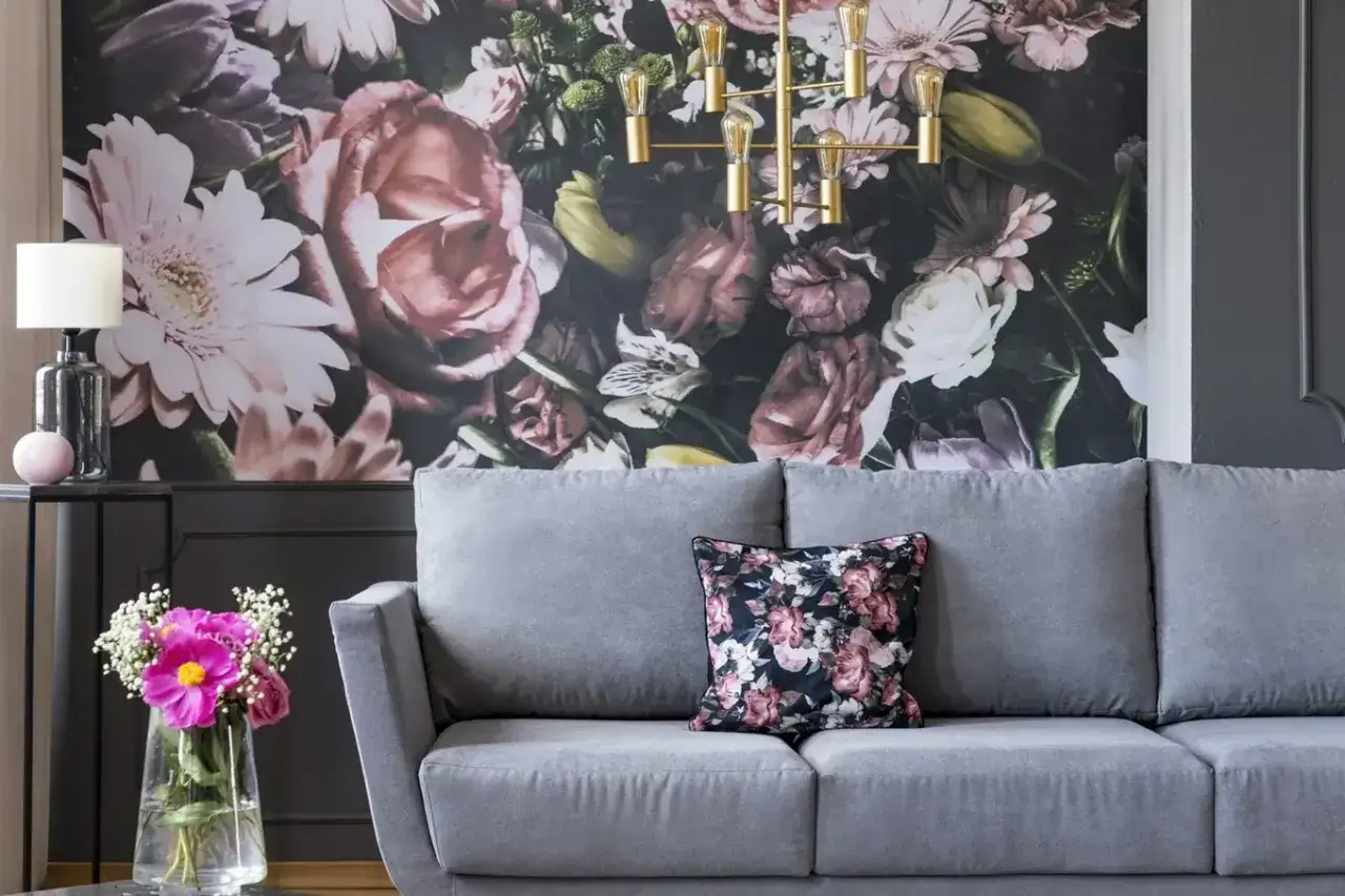 Szara sofa z poduszką w kwiaty, na tle bogatej fototapety. Idealna, by stworzyć przytulną atmosferę.
