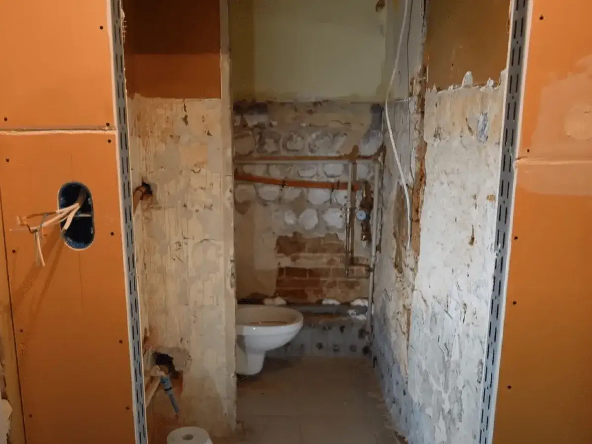 Remont łazienki w toku. Widać białą muszlę klozetową i instalacje. Ściany przygotowane pod płytę GK do łazienki.
