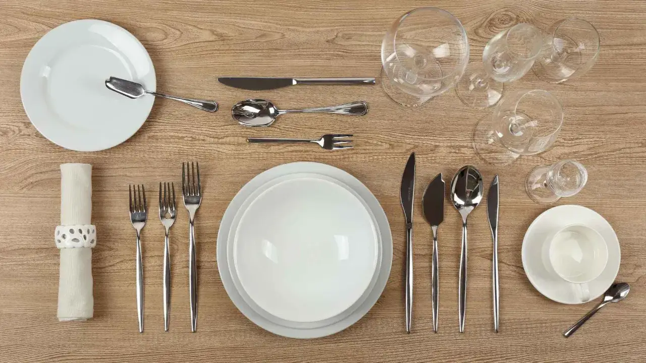Un dressage de table à la française impeccable : assiettes blanches, couverts brillants, verres à pied et serviette élégamment pliée.