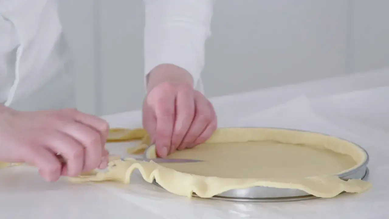 Préparation de la pâte pour une recette biscuit noisette. Les mains ajustent la pâte dans un moule à tarte.