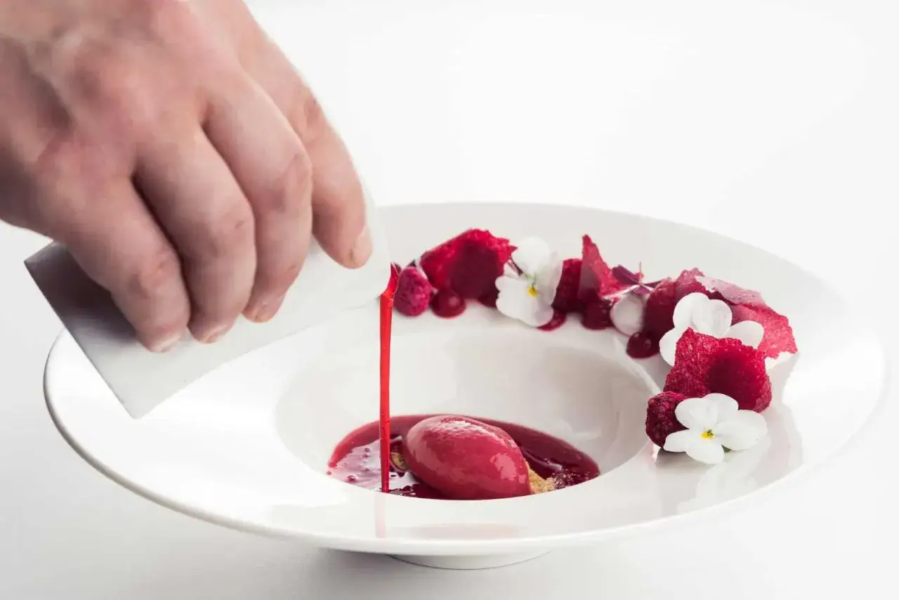 Wykwintny deser w restauracji z gwiazdką Michelin: malinowy sorbet z sosem i jadalnymi kwiatami, polany przez kucharza.