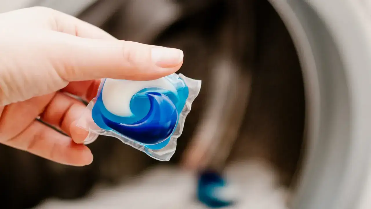 Mano sostiene una cápsula de detergente azul y blanca lista para usar en la lavadora.