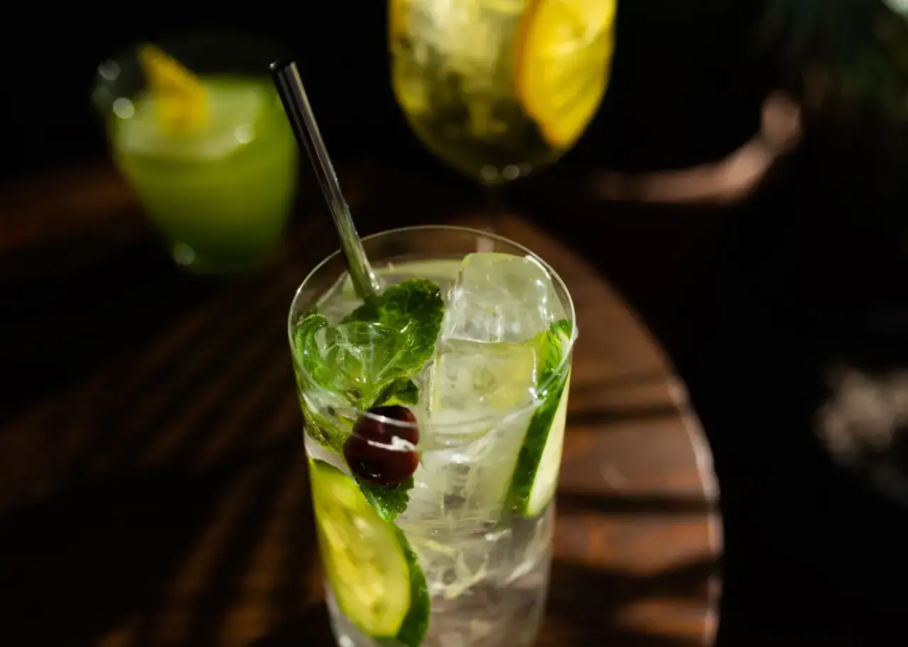 Orzeźwiający drink z ogórkiem, miętą i wiśnią, z lodem i słomką. W tle inne napoje.