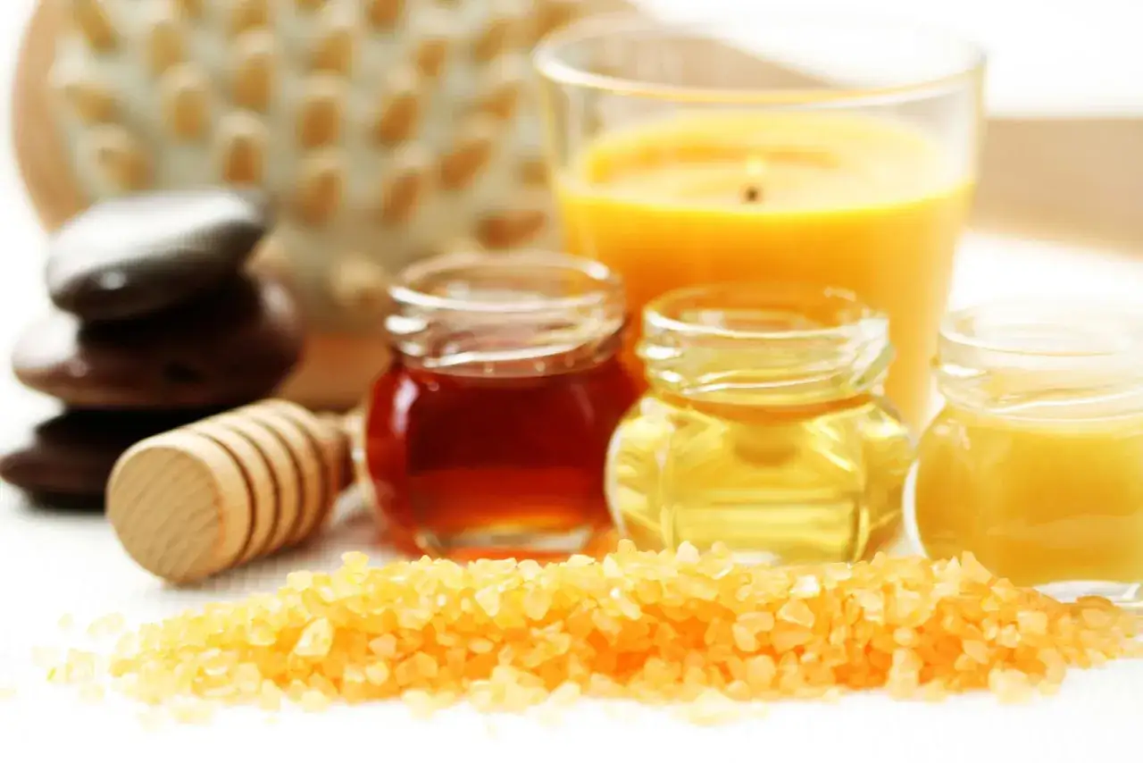 Ingredientes para un exfoliante corporal casero: sales, miel, aceites y una vela aromática.