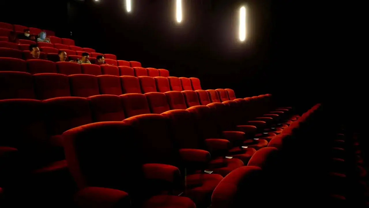 Czerwone fotele w kinie, widok na teatr Palladium plan widowni. Kilka osób siedzi w pustej sali.
