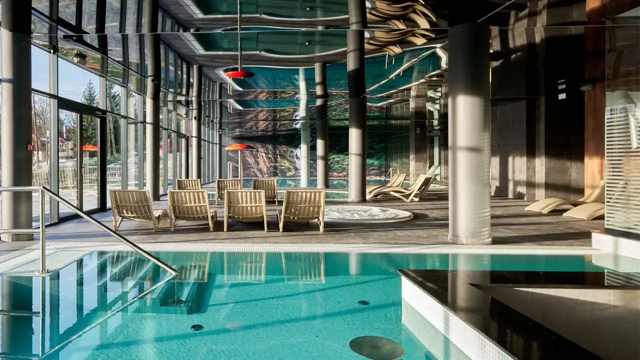 Basen z turkusową wodą i leżakami w nowoczesnym hotelowym spa.