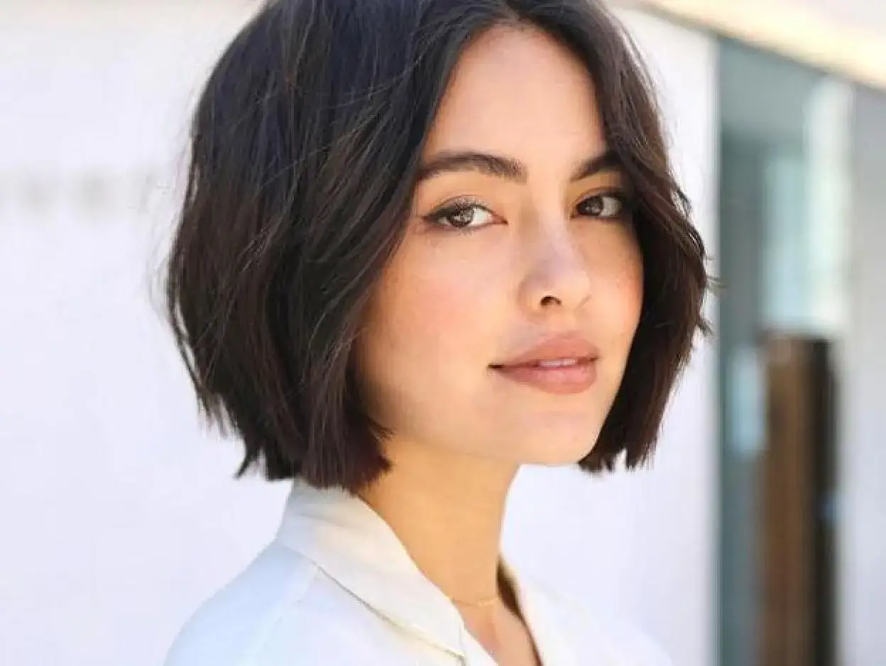 Mujer con un moderno corte de pelo bob oscuro y ondulado, luciendo un estilo chic y juvenil.