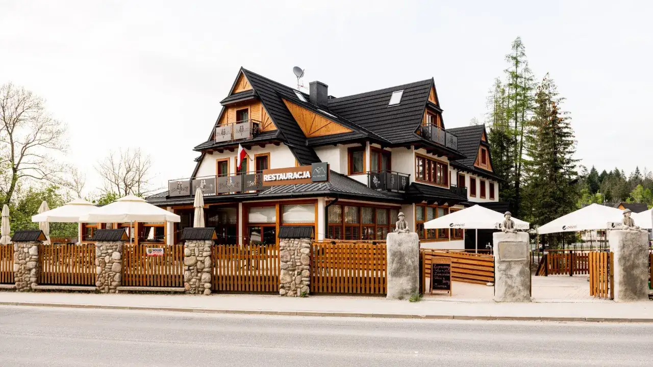 Szukasz miejsca, gdzie zjeść w Kościelisku? Ta restauracja z drewnianym ogrodzeniem i białymi parasolami zaprasza na góralskie smaki.