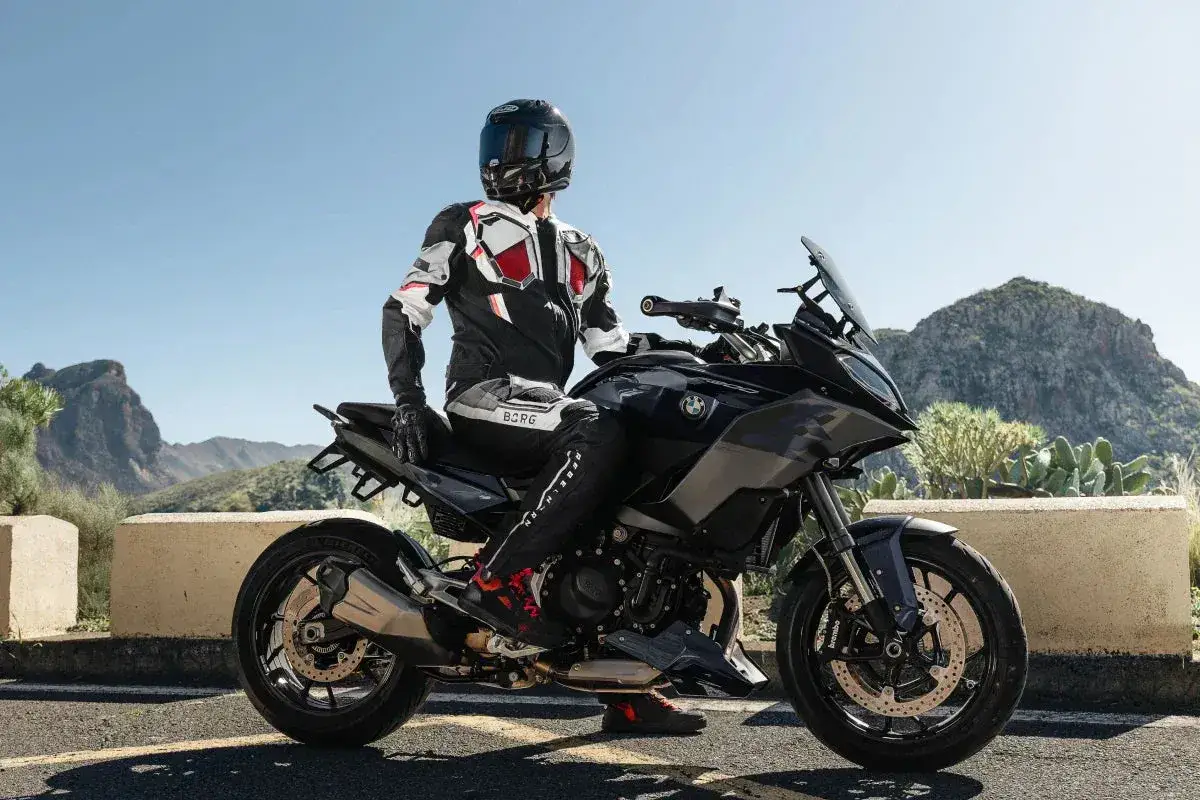 Motocyklista w kombinezonie na czarnym motocyklu BMW, gotowy do podróży po górskich drogach. Wśród wielu marek motocykli, ta prezentuje się imponująco.