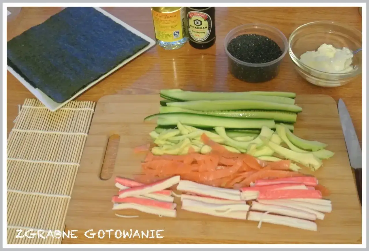 Pokrojone składniki do sushi: ogórek, łosoś, paluszki krabowe, awokado, sezam, sos sojowy, ryż i nori.