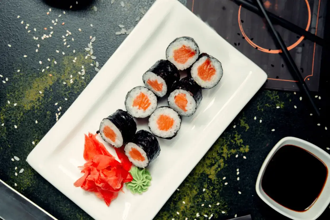 Pyszne hosomaki z łososiem, podane z imbirem i wasabi na białym talerzu.