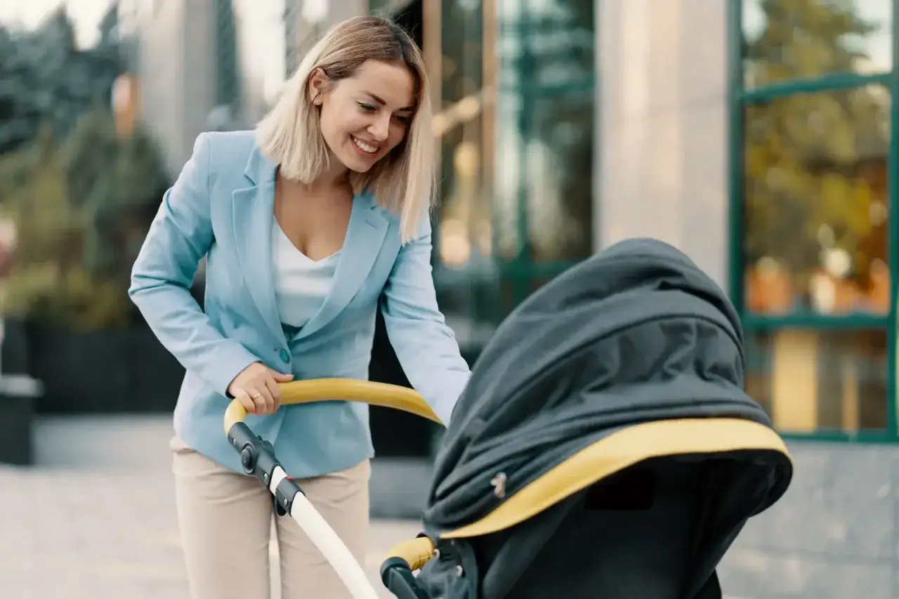 Uśmiechnięta kobieta w eleganckim stroju, z wózkiem dziecięcym, symbolizuje szukanie pracy dla matki po długim urlopie macierzyńskim i powrót na rynek.