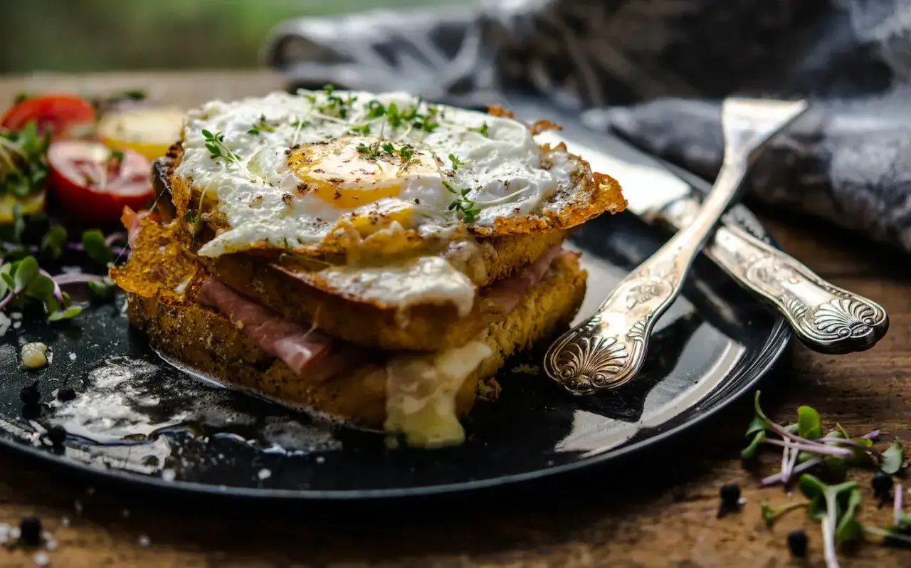 Un croque-madame gourmand, un des plats typiques parisiens, avec un œuf au plat, jambon et fromage fondant, servi avec des tomates et des pousses.
