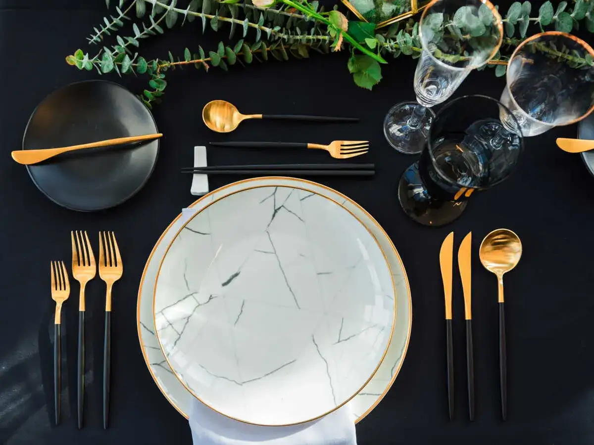 Une table élégamment dressée pour un repas. On peut y voir comment **poser les couverts à la française**, avec des assiettes marbrées, des verres et des couverts dorés et noirs.