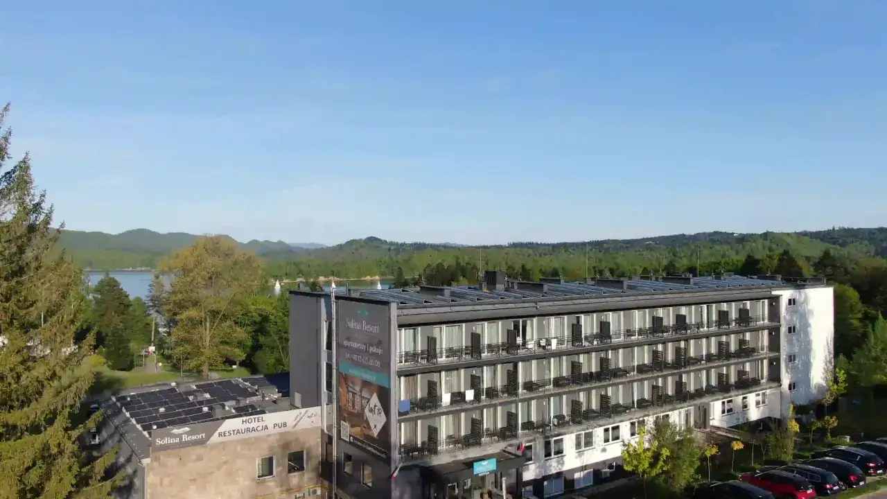 Widok na hotel Solina Resort & Spa z apartamentami i pokojami, otoczony zielenią, z jeziorem Solina w tle.