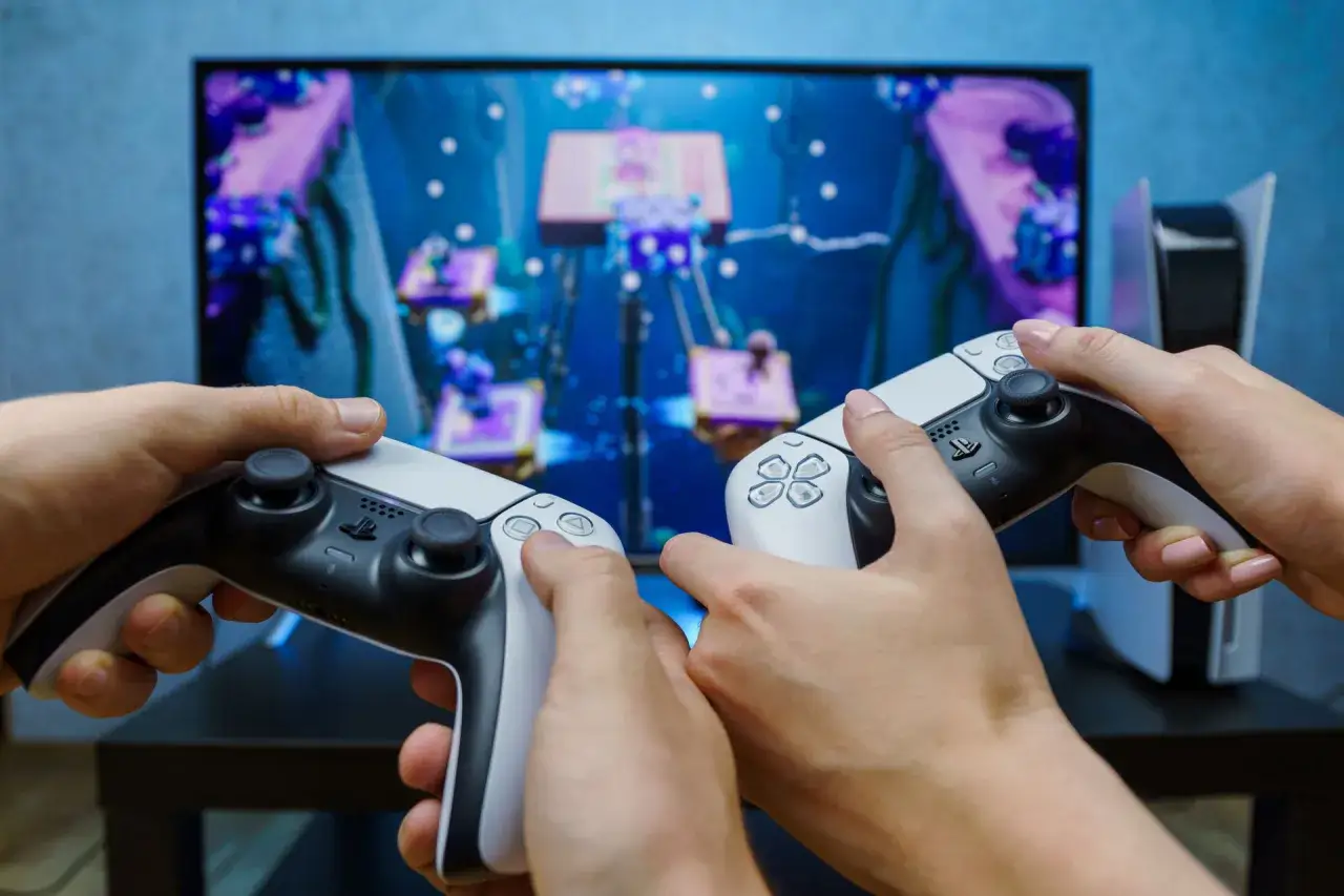 Dwie osoby grają w grę na konsoli PlayStation 5, trzymając kontrolery DualSense.