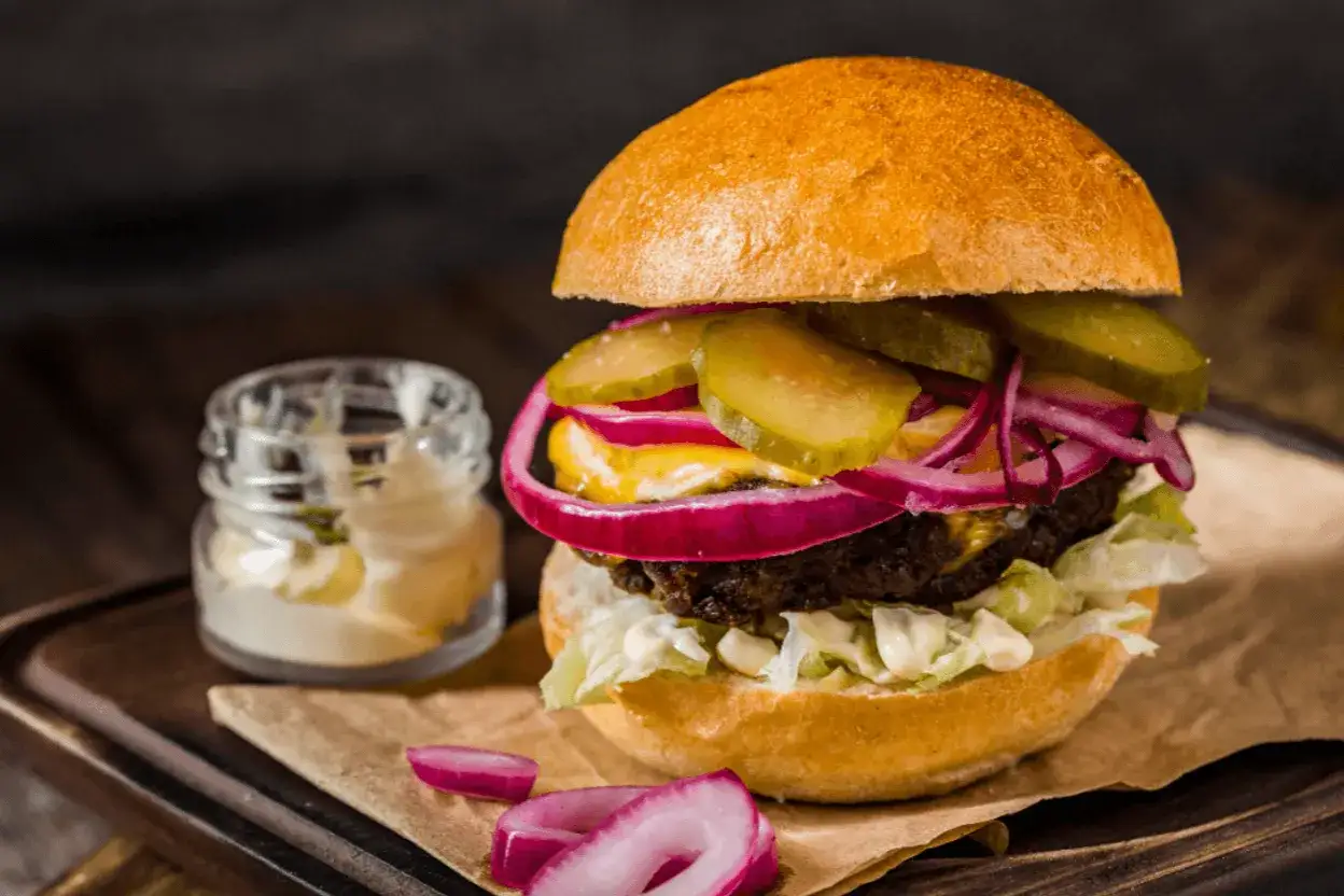 Soczysty burger z ogórkiem, czerwoną cebulą i majonezem, idealny do przygotowania, jak smażyć burgera na patelni.