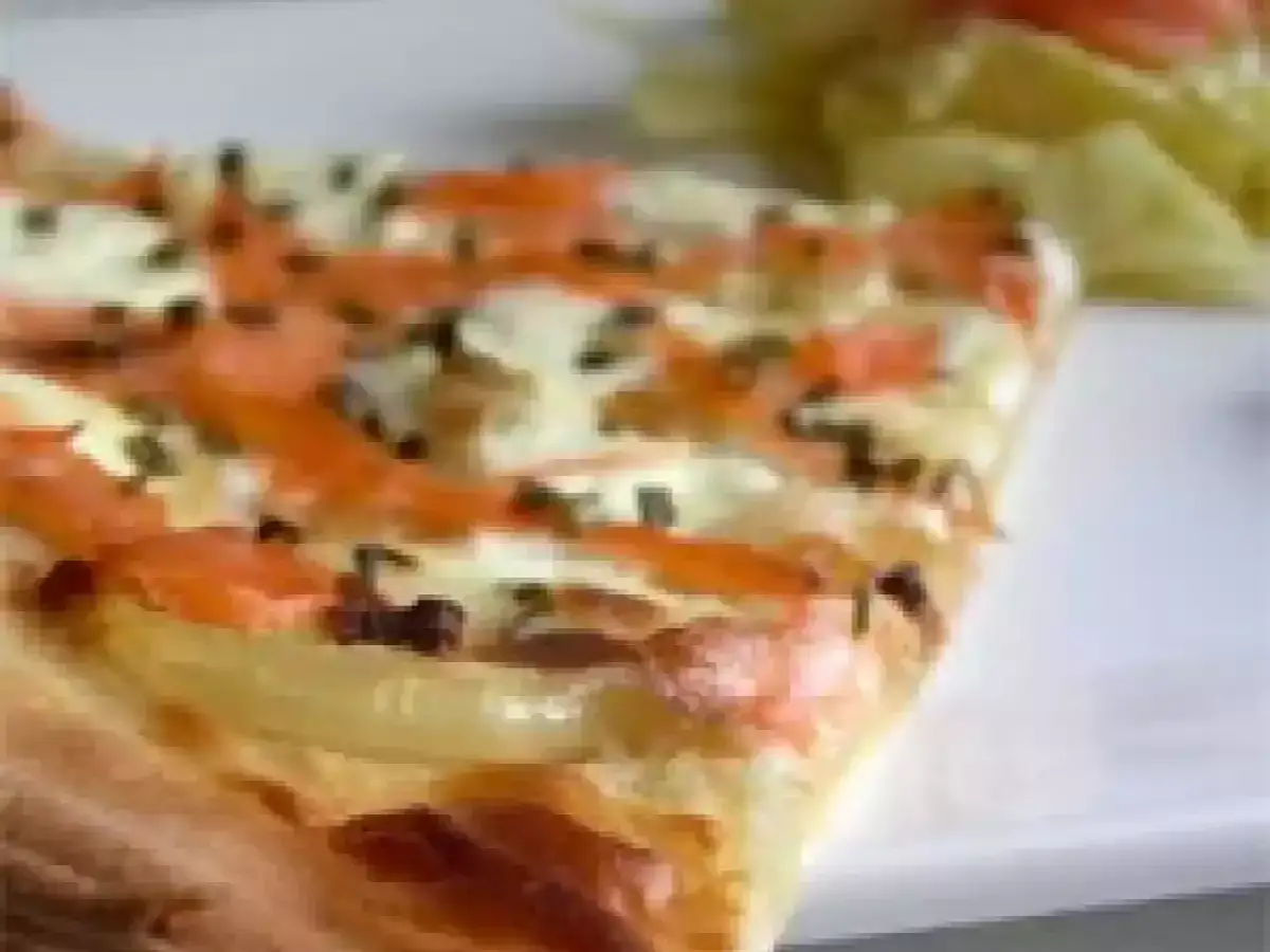 Tranche de flammekueche saumon, oignons et fromage, avec une salade verte en arrière-plan.